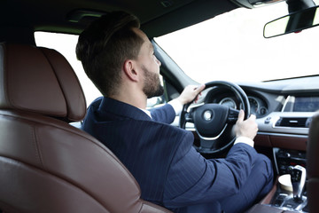 businessman sits at the wheel in his car and looks at the road