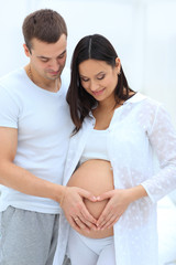 husband and pregnant wife with folded hands in the shape of a heart on his tummy