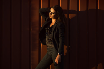 Portrait of pretty serious business woman is wearing black official clothes near wooden wall