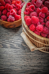 Bowl and bucket with red raspberries on wooden board