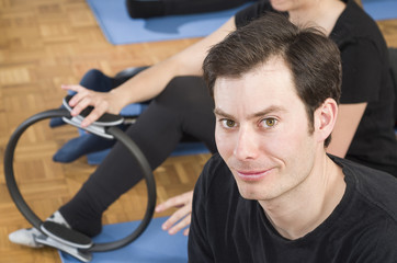 Diverse group of people in a gym class lying in a receding row on mats doing Pilates exercise. Man looking at camera