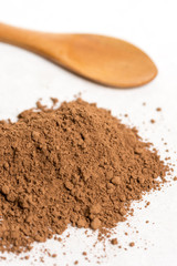 Brown cocoa powder with wooden spoon isolated above white marble background