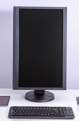 Black blank pc monitor turned vertical and keyboard on desk.