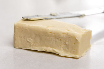 Slice of butter with kitchen knife on the white marble background table