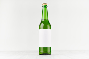 Green longneck beer bottle 500ml with blank white label on white wooden board, mock up. Template for advertising, design, branding identity.