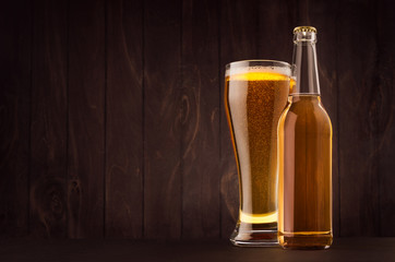 Transparent beer bottle and glass weizen with golden lager on dark brown wood board, copy space, mock up. Template for advertising, design, branding identity.