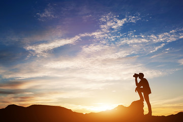 Man looking through binoculars at sunset.