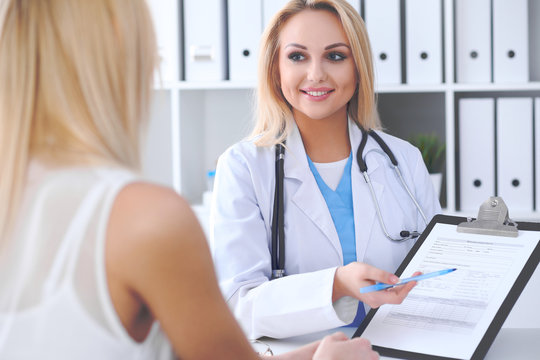 Doctor and  patient  discussing something while physician pointing into medical history form at clipboard