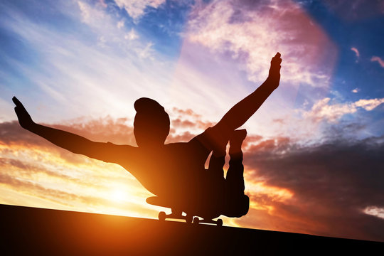 Young man lying on skateboard at sunset.