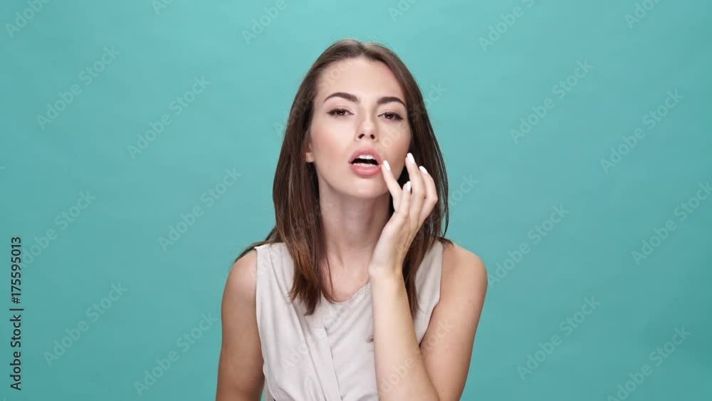 Sticker smiling brunette woman in t-shirt corrects her make up and hairstyle while looking at the camera ove