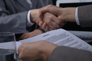 Close-up of contract paper with business handshake at the background. Successful negotiation or meeting concept. Low key lighting 
