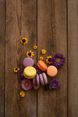 Colorful Macarons and flowers on wooden table background. French dessert with fresh flowers. Top view. Autumn concept