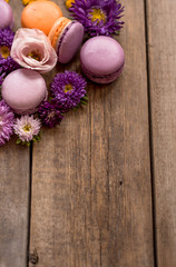 Obraz na płótnie Canvas Colorful Macarons and flowers on wooden table background. French dessert with fresh flowers. Top view. Autumn concept