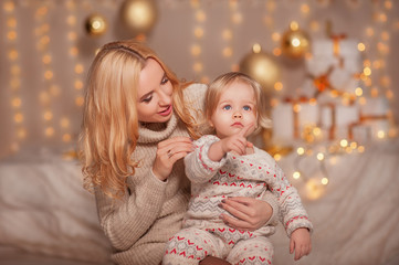 Merry Christmas and Happy holidays! Small kid girl with mom sitting in decorated room with gifts and lights and enjoying. Daughter and mother spending holiday together. Family New Year concepts