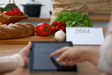 Close-up of four human hands are gesticulate over a tablet in the kitchen. Friends having fun while...