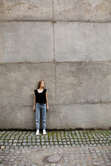 Young woman in jeans outdoors standing agaict grey wall. Girl in casual clothes, standing in the street.