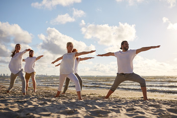 group of people making yoga exercises on beach