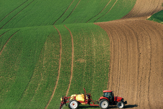Modern Red Tractor Plowing And Spraying On Field. Small Tractor Working On A Colorful Spring Field.Agriculture Tractor Creating Abstract Brown Background Texture.Rural Scenic Landscape.Czech Republic