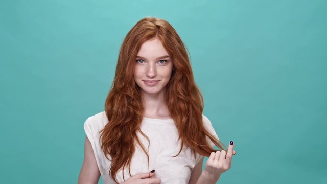 Smiling ginger woman in t-shirt posing and looking at the camera over turquoise background