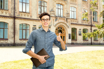 Fototapeta premium Young man in the glasses with a digital tablet in hand on a university background. Male student.