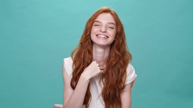 Laughing ginger woman in t-shirt looking at the camera over turquoise background
