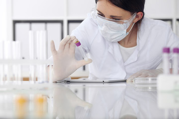 Close-up of professional female scientist in protective eyeglasses making experiment with reagents...