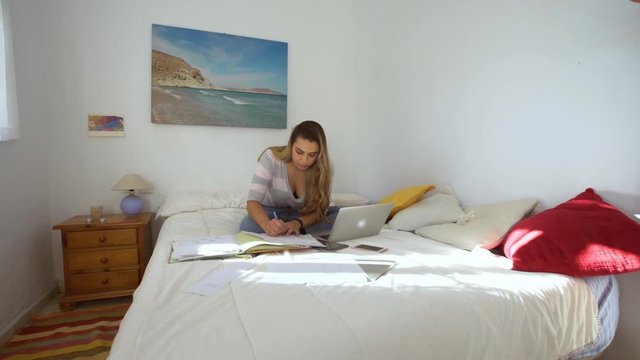 A beautiful woman studiying in the bedroom with laptop