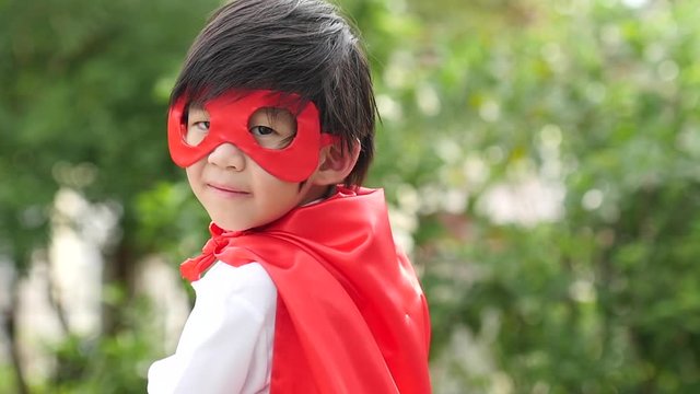 Asian child in in Superhero's costume playing in the park slow motion 