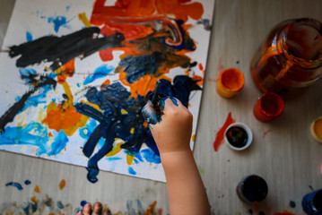 The child draws colored gouache with his fingers and brush on paper