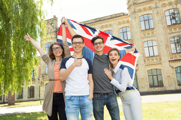 Group of students holding a flag of Great Britain on the university campus background.