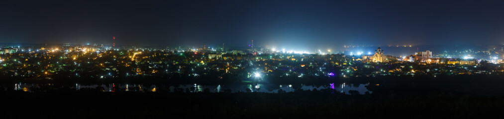The bright lights of the city streets in the background of the night sky. Panoramic view of residential areas.