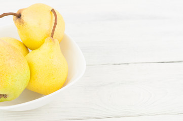 Heap of fresh ripe yellow whole pears in white ceramic bowl on old rustic white wooden table