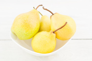 Heap of fresh ripe yellow whole pears in white ceramic bowl on old rustic white wooden table