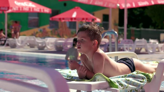 Boy resting and taiking sunbathe on a lounger in the aquapark near the pool