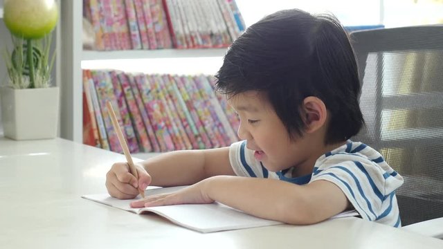 Unhappy Asian child working on hard homework at home alone 