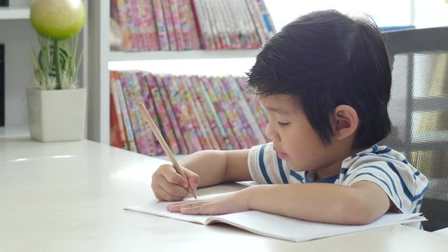 Little Asian child  using a pencil to write on notebook at the desk