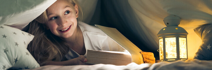 Girl under the covers reading book - obrazy, fototapety, plakaty