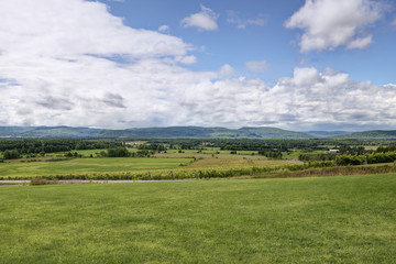 Fototapeta na wymiar Summer landscape. Green fields, blue sky and mountains in background.