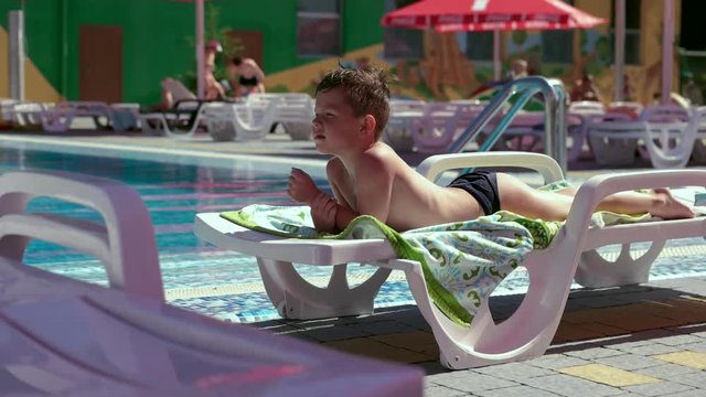 Boy resting and taiking sunbathe on a lounger in the aquapark near the pool