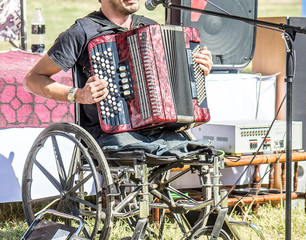 A disabled person without legs in a stroller plays the accordion