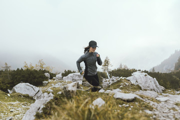 Young fit athletic woman running high in the mountains on rocky trail.