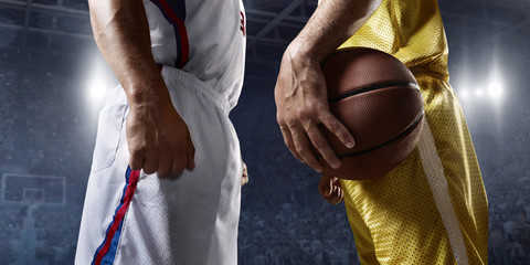 Two basketball players stands face-to-face before the game on big professional arena. Players wears unbranded uniform. One player holds a basketball ball.