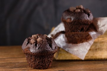 Two fresh unwrapped chocolate chunks muffins on dark wood table