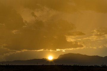 Obraz premium sun setting behind a mountain range with crazy golden hour light and storm clouds overhead