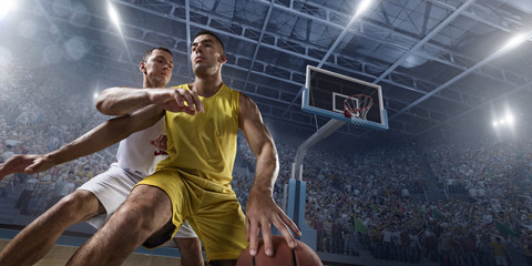Two basketball players fight for the basketball ball on big professional arena. Player wears unbranded clothes. © Alex