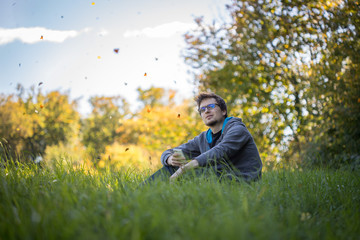Junger Mann sitzt im Gras, tanzende Blätter, entspannt und nachdenklich, Textfreiraum