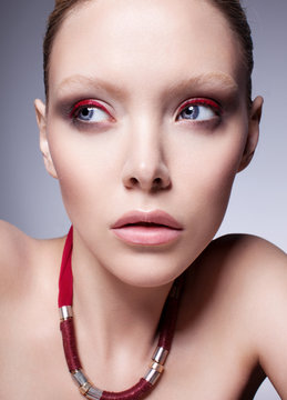 Blond model with red eyeshadow and blue eyes. Beautiful make-up. Gray studio background.