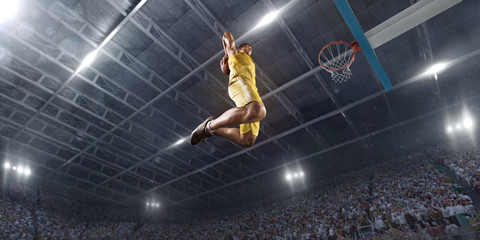 Basketball player makes slam dunk on big professional arena. Player flies through the air with the...