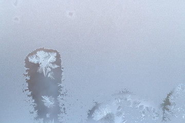 Winter frosty window glass, wave thawed spots with snowflakes inside and copy space.