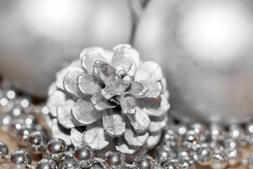 Abstract silver christmas background. Close-up colored pine cone, thread with beads and blurred balls in background.